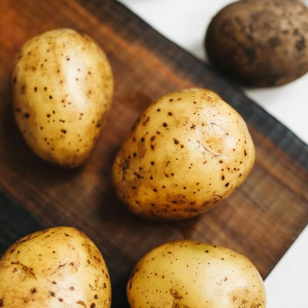 pexels-photo-4110462-4110462 Close-up of fresh potatoes on a wooden board, highlighting their natural texture.